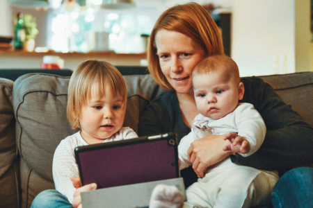 mother with toddler and baby on a sofa looking together at a tablet
