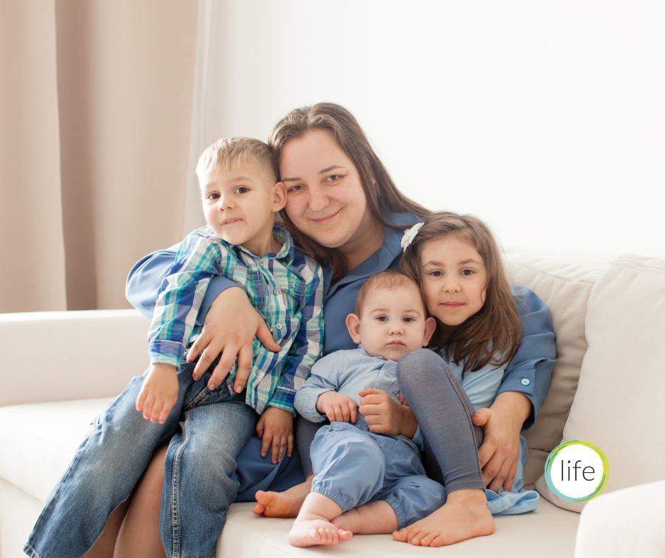 Mother and three children on sofa in blue jeans and shirts smiling - Life charity blog on two-child benefit cap being lifted in UK Autumn budget 2025