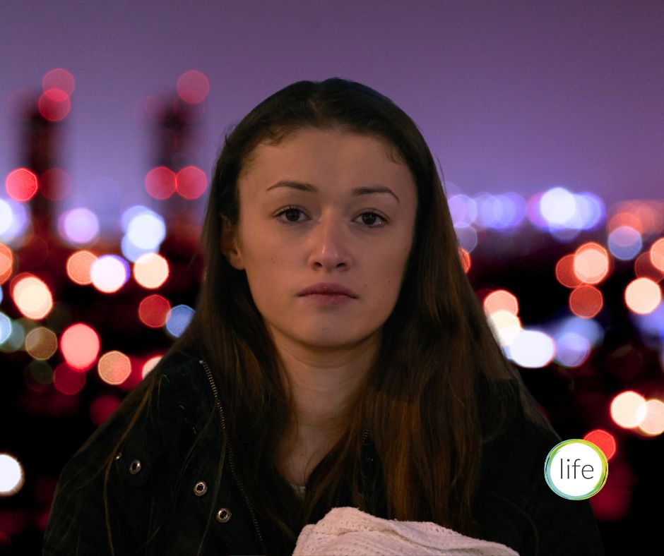 Woman cradling baby in cold dusk of city